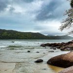 Praia da Enseada, em Ubatuba, com águas calmas, faixa de areia e morros cobertos pela Mata Atlântica