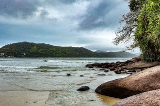Praia da Enseada, em Ubatuba, com águas calmas, faixa de areia e morros cobertos pela Mata Atlântica