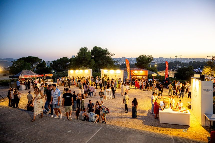 Público se reúne ao entardecer em um festival ao ar livre com barracas de comida e clima festivo.