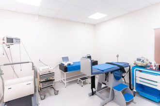 Sala de exame médico limpa e equipada com maca, armários e instrumentos de atendimento.